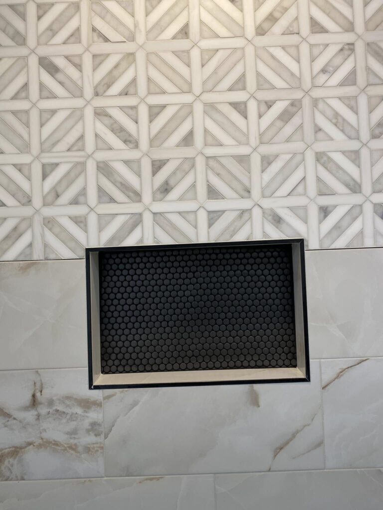 Shower niche with black penny tile under a geometric marble accent, Chattanooga, TN by Palacios Installation